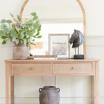 A stunningly crafted brass-framed arched top mirror. It sits on a pine console table.