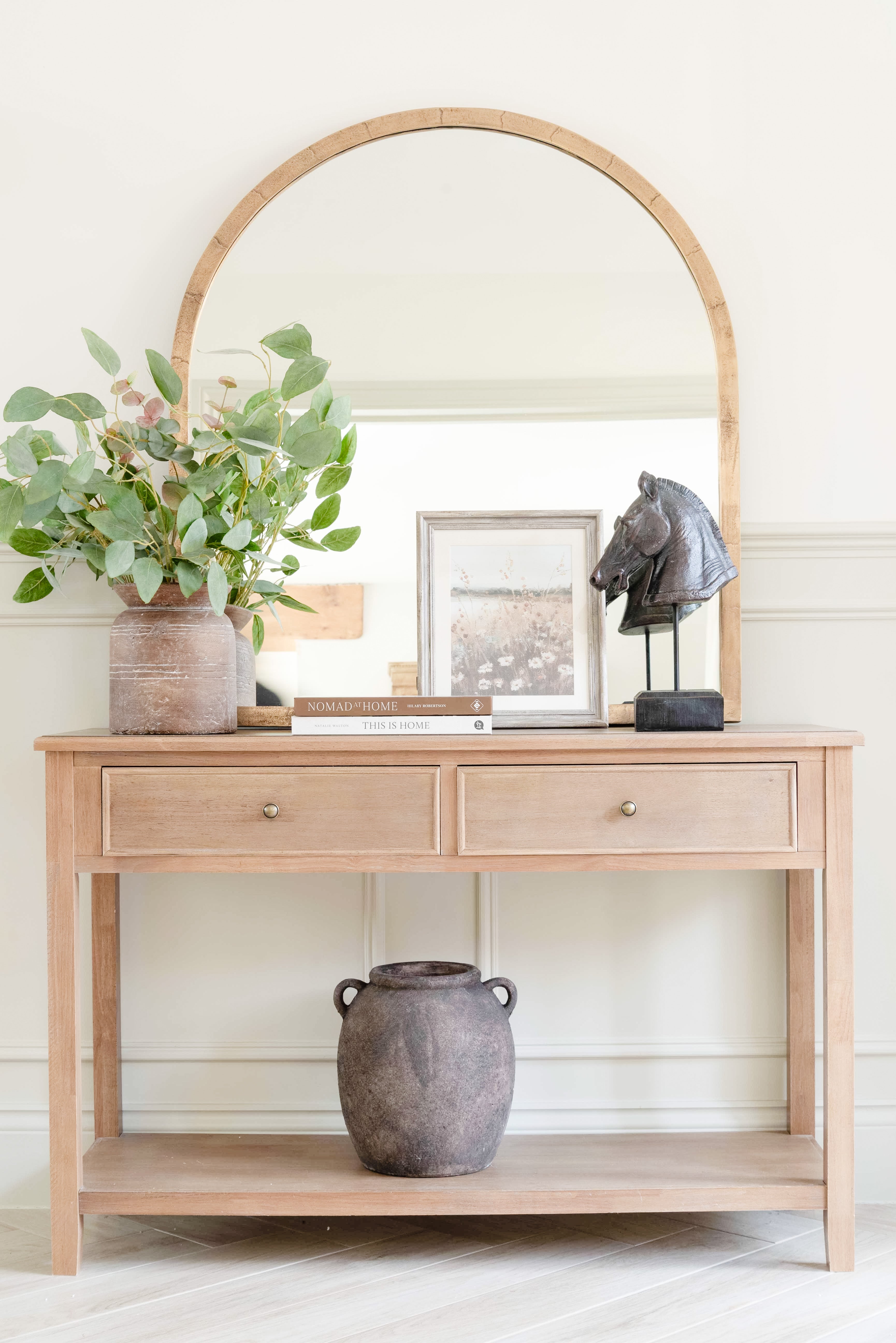 A stunningly crafted brass-framed arched top mirror. It sits on a pine console table.