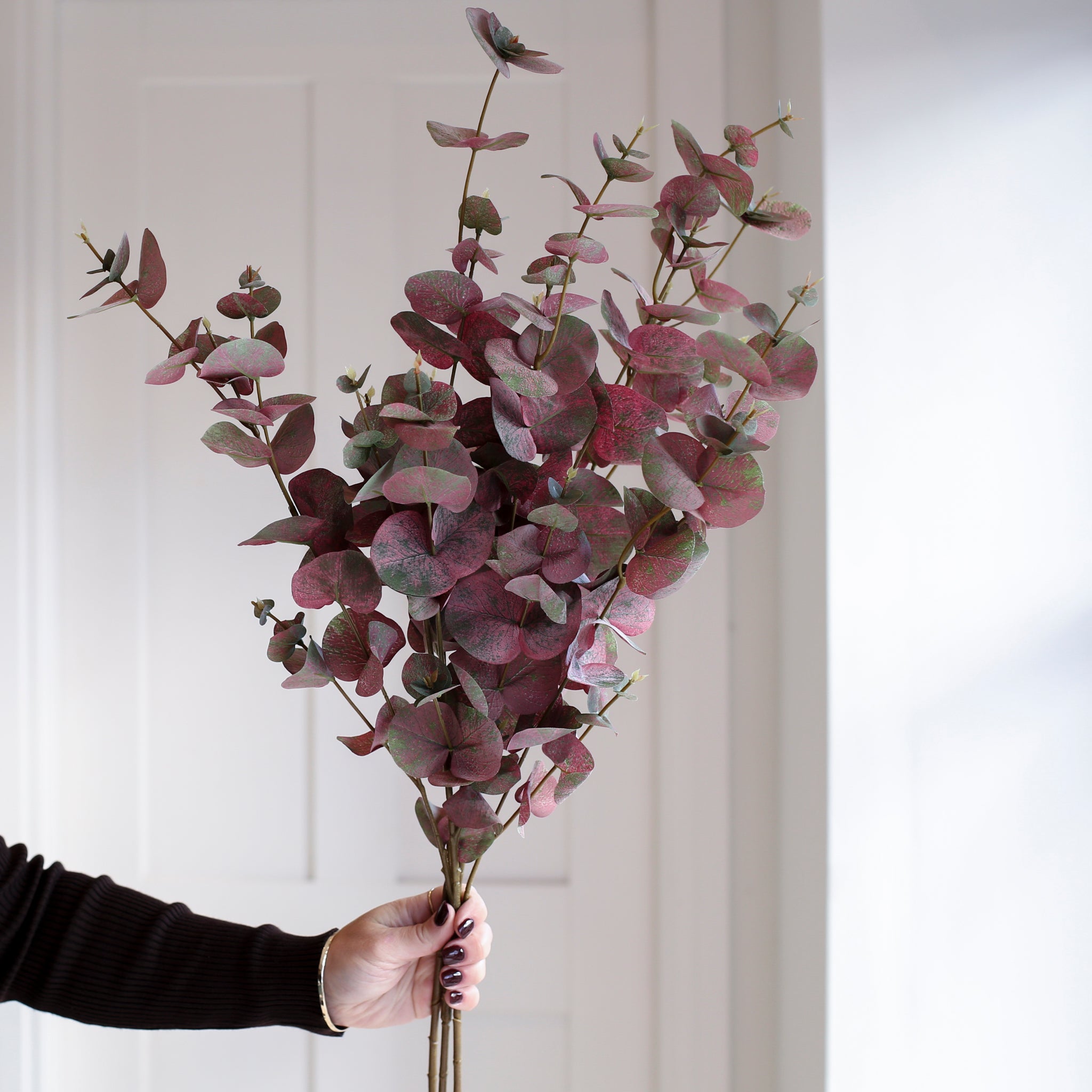 A single stem of lifelike faux eucalyptus in burgundy and green