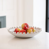 Shallow white ceramic bowl with bobble detailing around the rim. Holds a stack of small apples