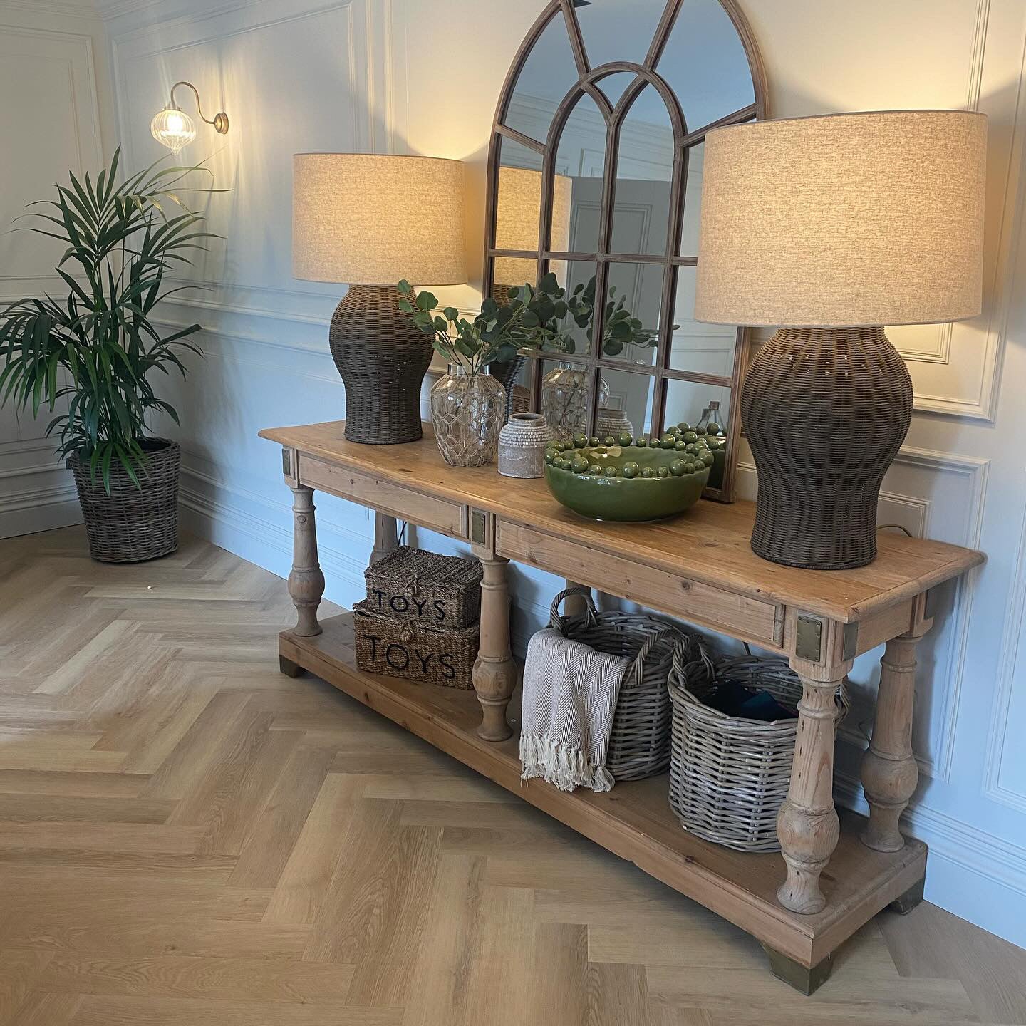 Two large rattan lamps with linen shades on either side of a mirror on a console table